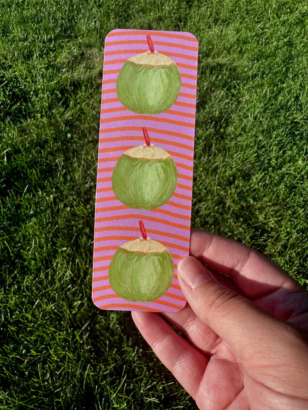 Coconut bookmark with three green coconuts and red straws on lavender and coral stripe background