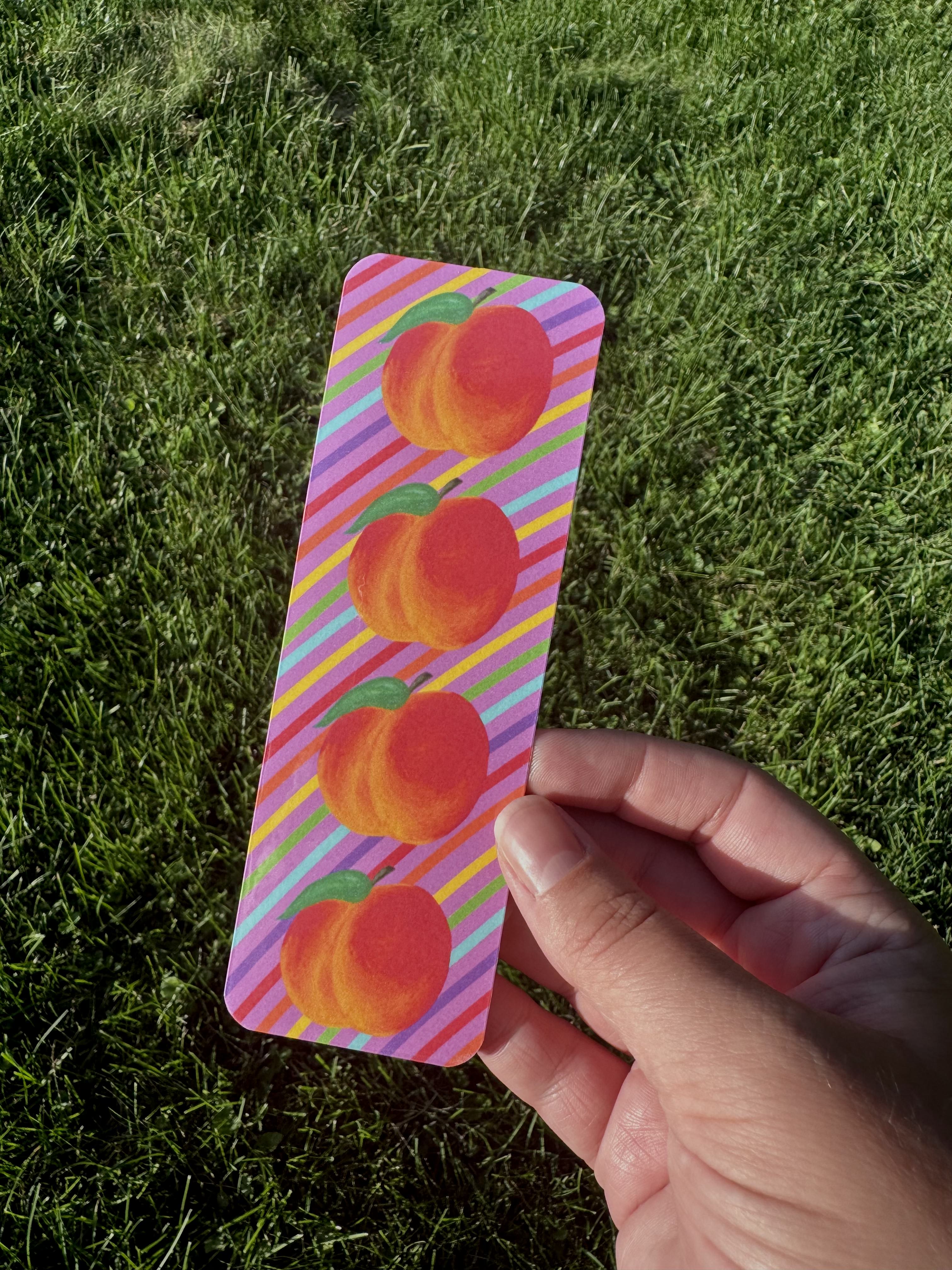 Peach bookmark with three orange peaches and green leaves on multicolor diagonal stripe background